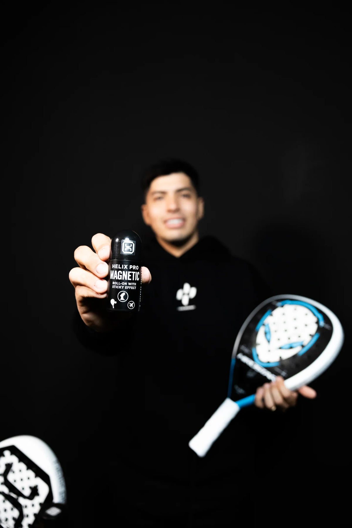 Padelspieler hält den Helix Pro MAGNETIC Roll-On vor schwarzem Hintergrund